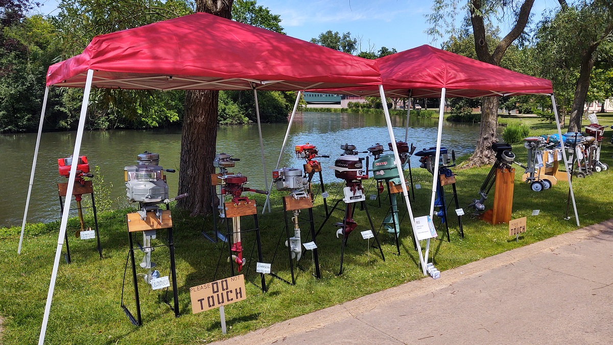 Outboard boat motors at Motor Muster 2022 in Greenfield Village Display of motors on stands under red tents in front of a lake or other body of water