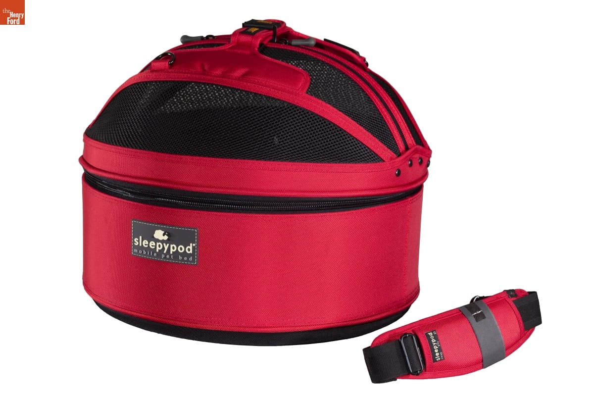 Red fabric carrier with domed black mesh top; handle (?) laying nearby