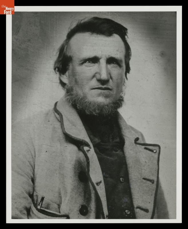 Head and torso of man with beard/sideburns around the edge of his face, wearing jacket
