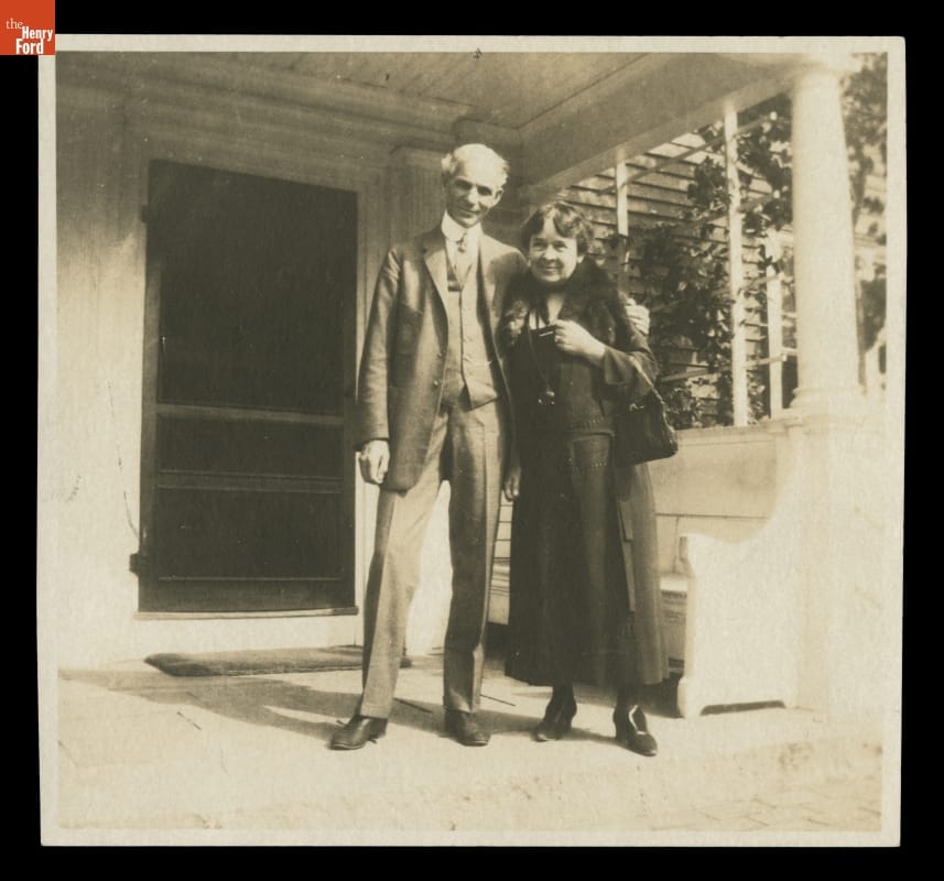 Black-and-white photo of man and woman standing on the porch of a building