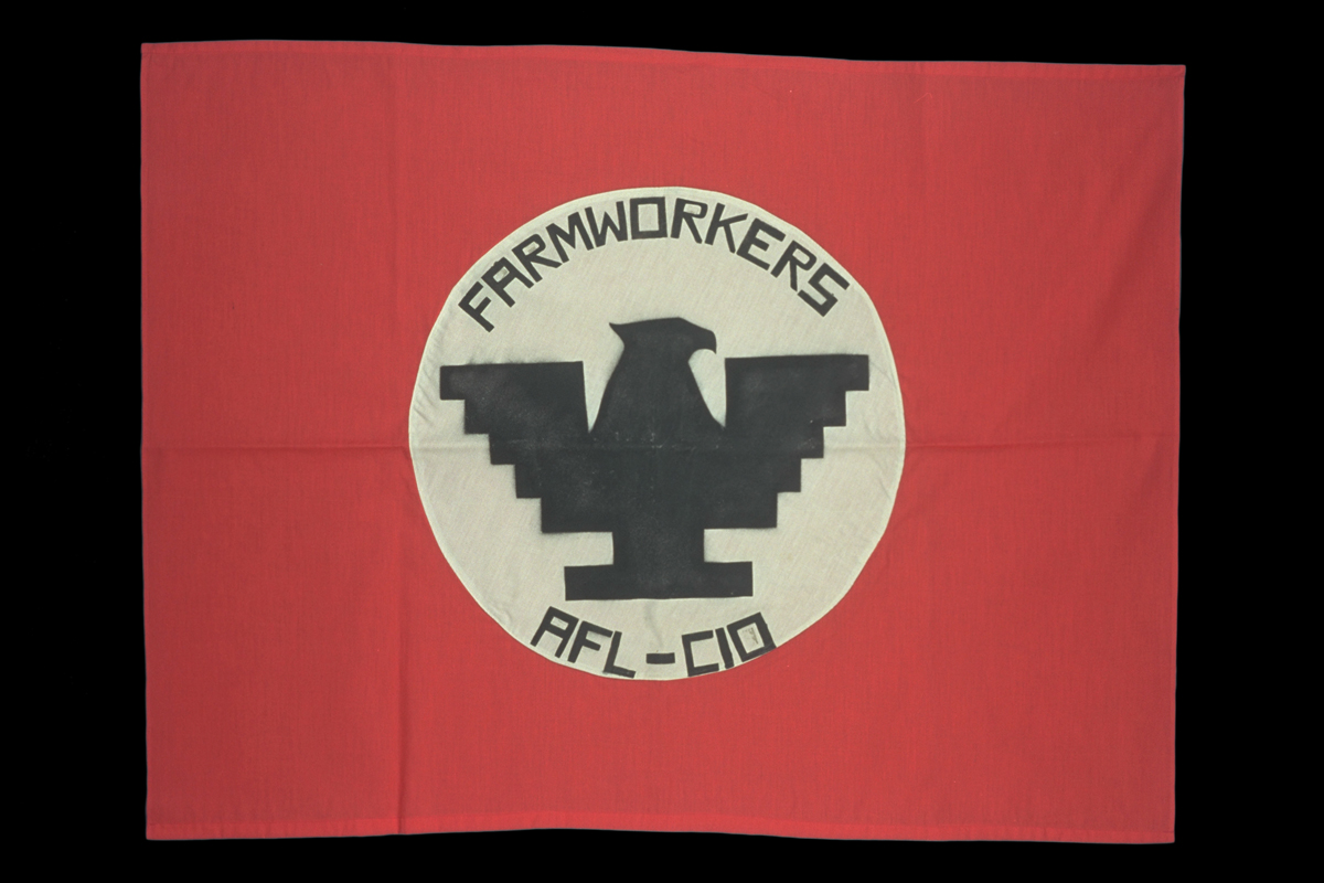 Red flag with white circle in middle containing stylized black eagle and text "FARMWORKERS AFL-CIO"