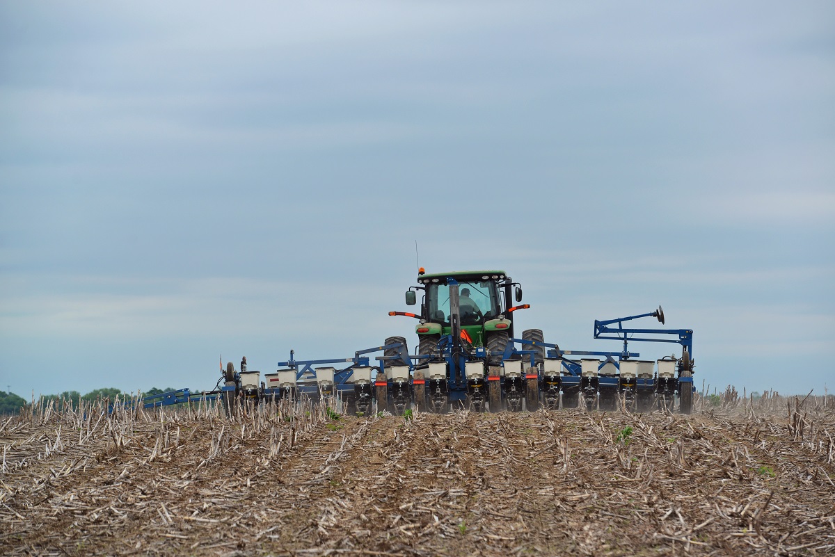 A Modern John Deere No-Till Planter Sowing Soybeans A green tractor trailing a long blue machine hitched behind it travels through a field of dirt and stubble
