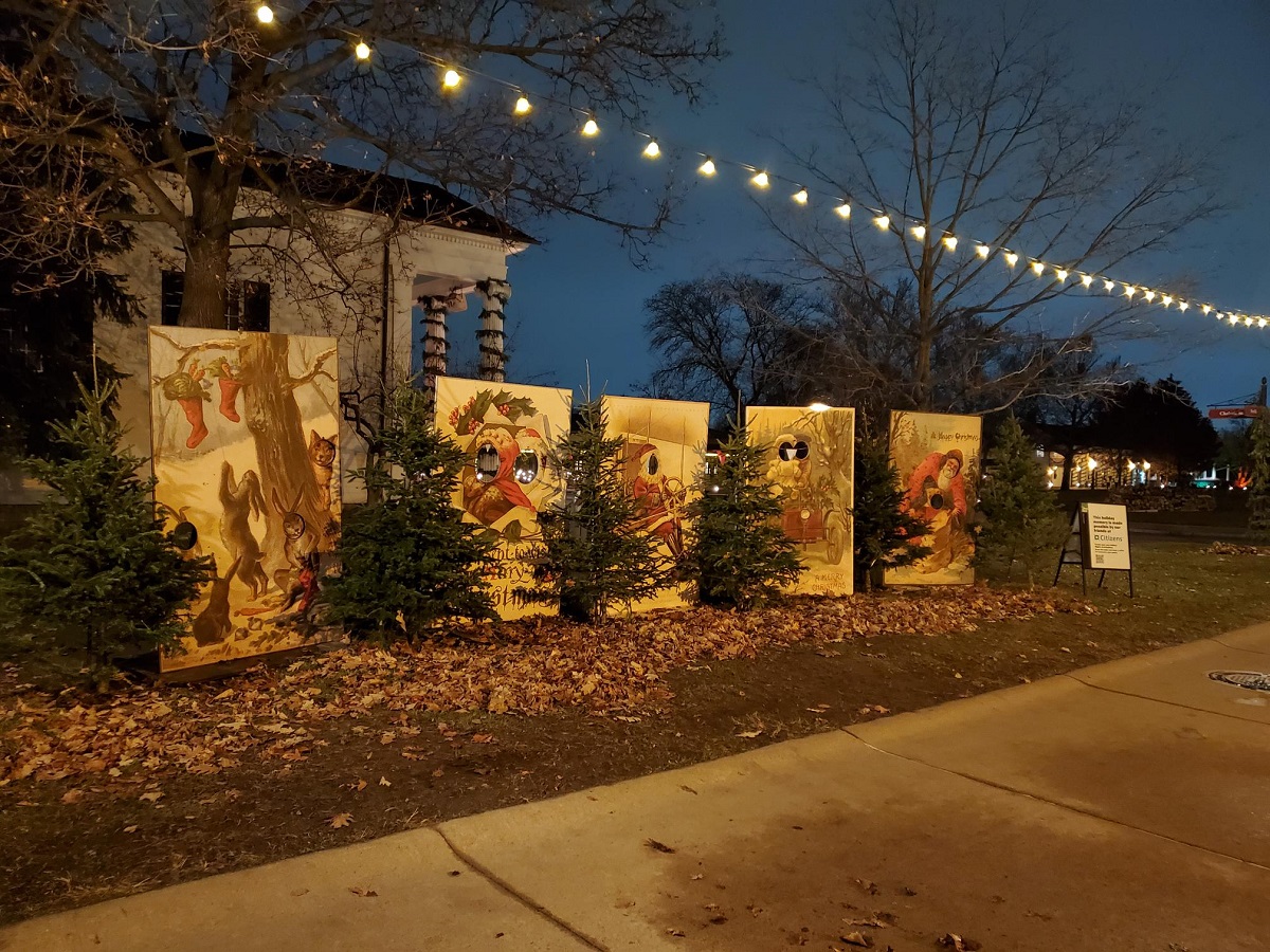 A row of large wooden backdrops with holes cut for people's faces stands in front of a building along a sidewalk