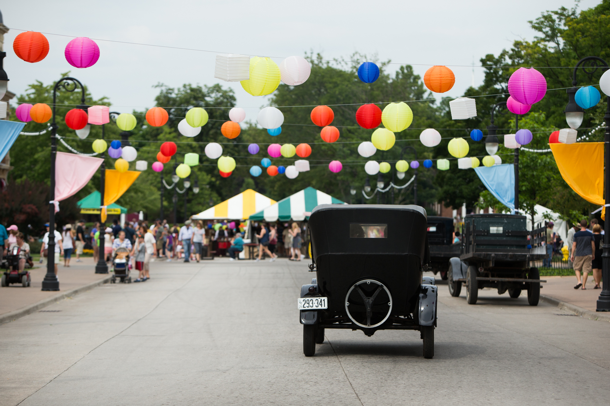 Antique car driving down a street festooned with balloons
