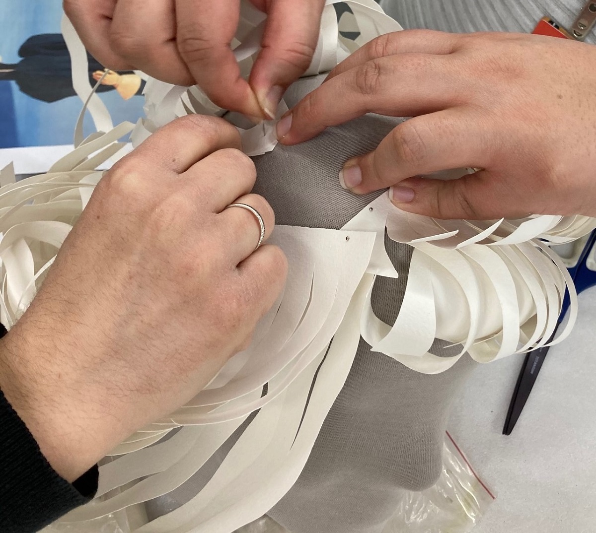 Three hands pinning curled white paper to a gray mannequin head