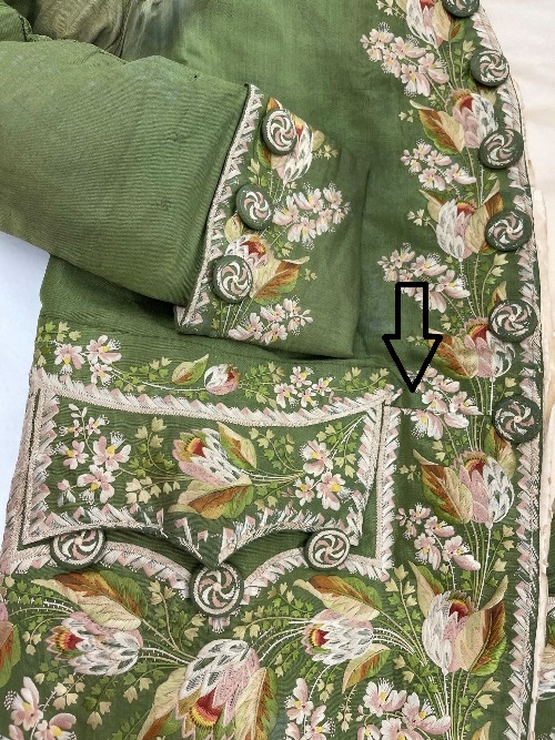 Detail of moss-green suit pocket and part of cuff with elaborate embroidery; an arrow points to a seam coming off the top of the pocket