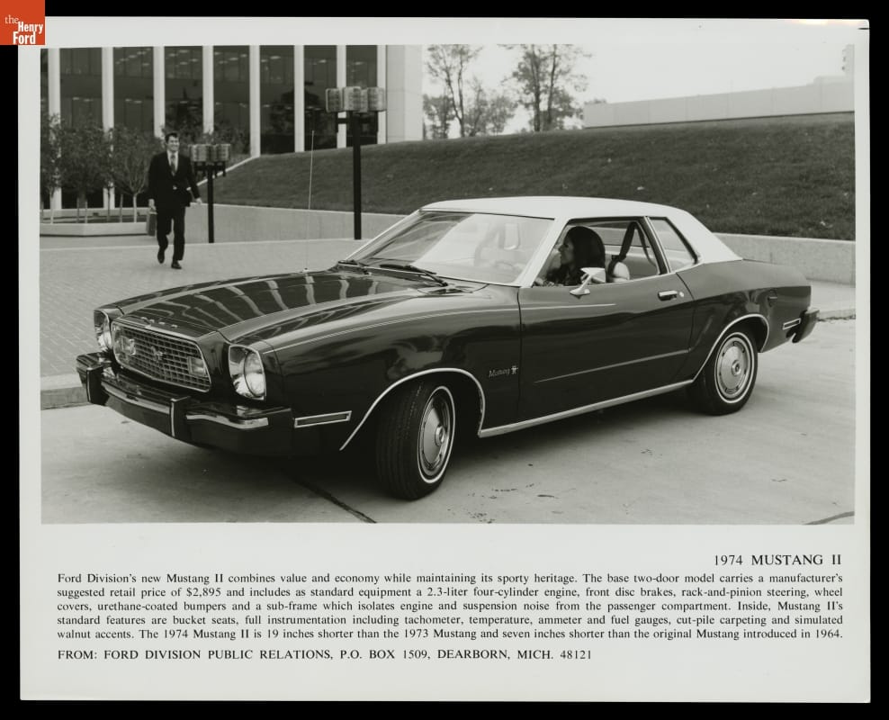 Publicity Photograph of the 1974 Ford Mustang II Black-and-white photo of car in front of building with concrete plaza and grass berm; one person is behind wheel and another in suit walks toward car