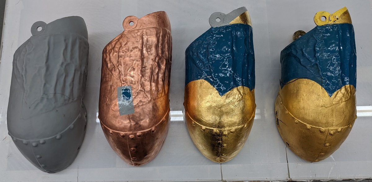 Four identical tubular shapes--left one gray, next one copper, third gold and blue, right semi-dull gold and blue