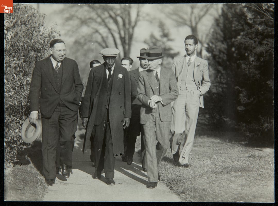 Group of men walk on a sidewalk between grass and trees