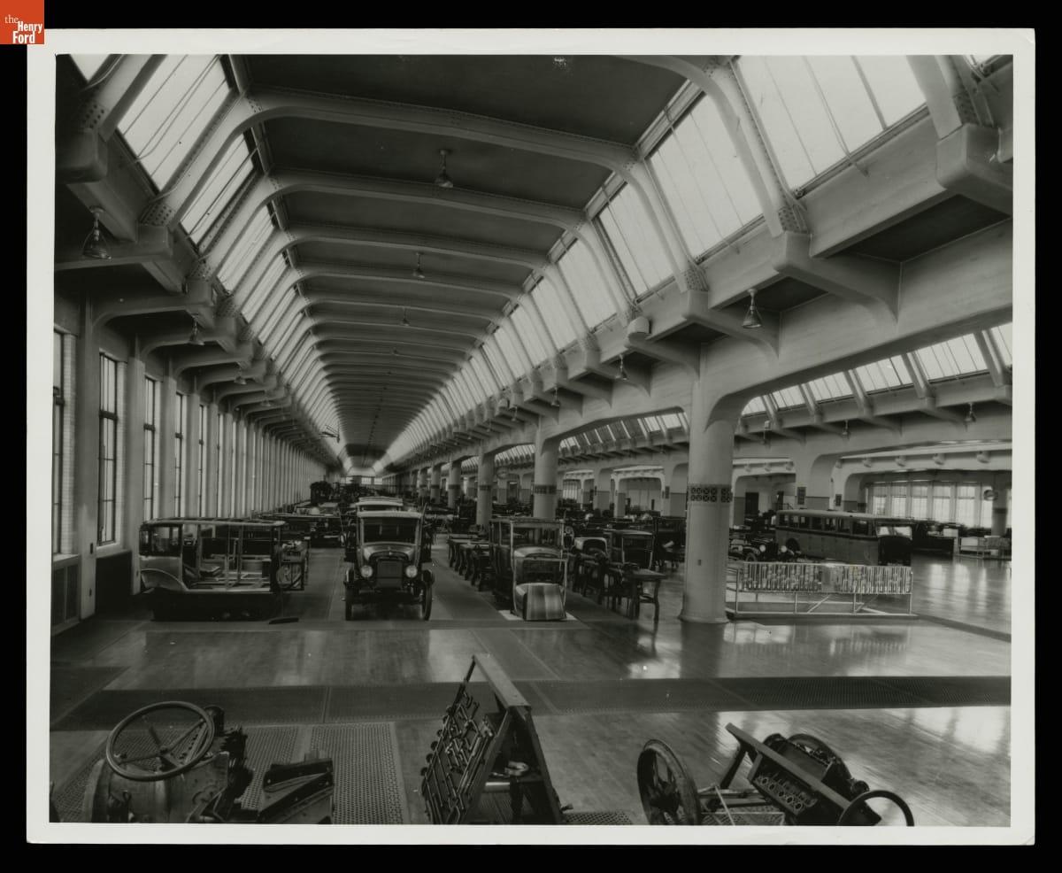 Cars and other objects stored in a vast, tall room with many windows 