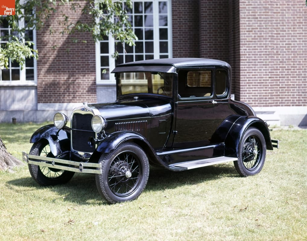 Black car on grass in front of a brick wall with windows