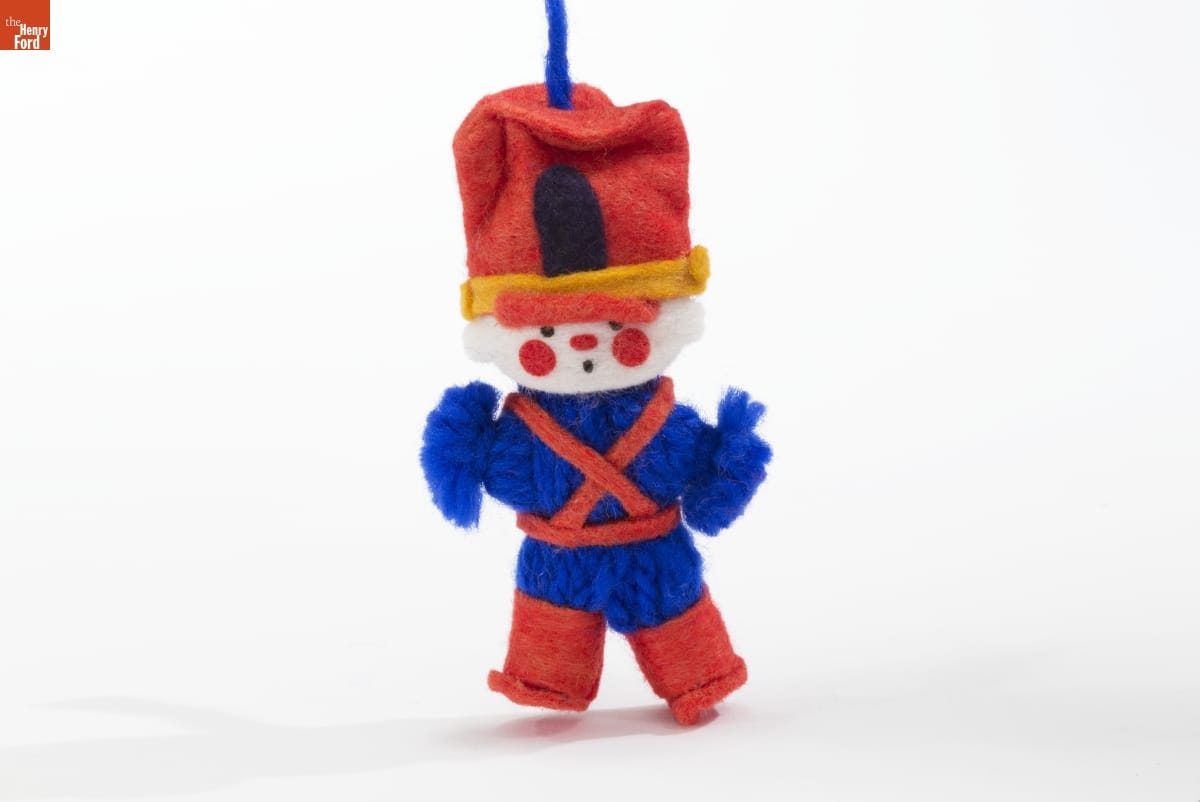 Toy soldier ornament with blue yarn body, red felt hat, suspenders, and boots, and white felt face
