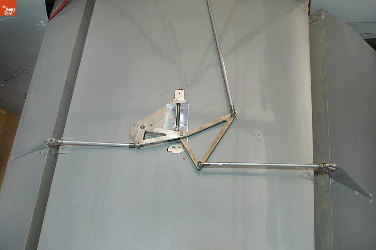 Close-up of gray plane wing with triangular metal pieces attached to long rods