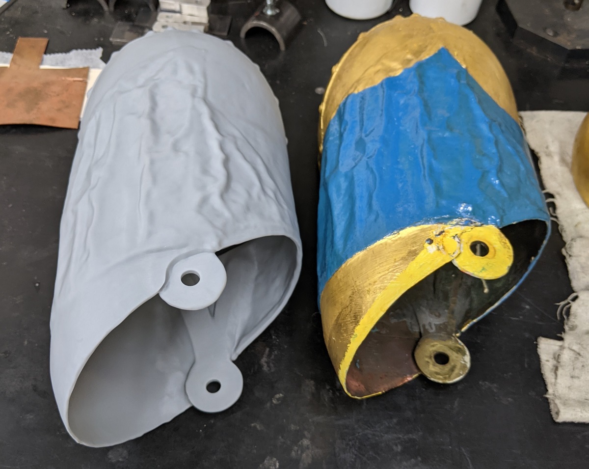 Two hollow shapes--one gray, one painted yellow and blue, sitting on a workbench