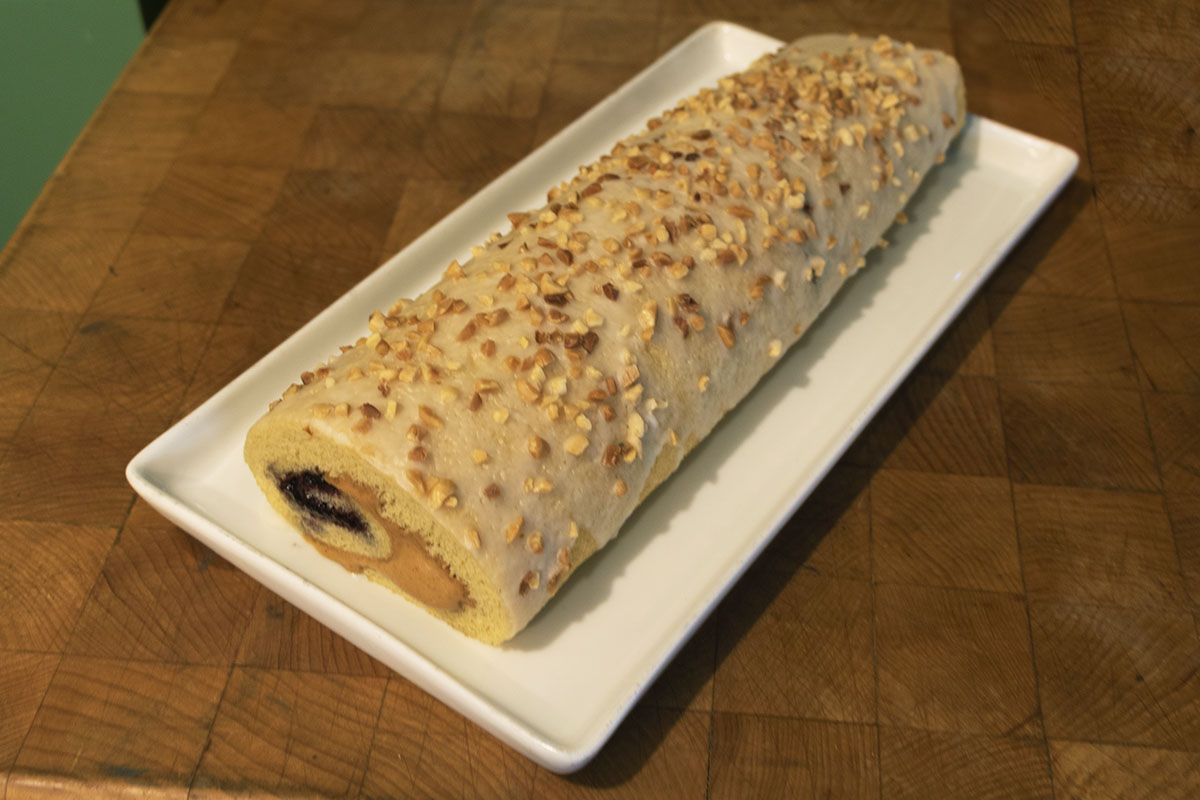 Rolled cake topped with peanuts and with peanut butter/jelly filling visible at end