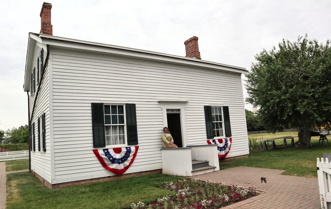 Woman sits on bannister on porch outside white, wooden, two-story house