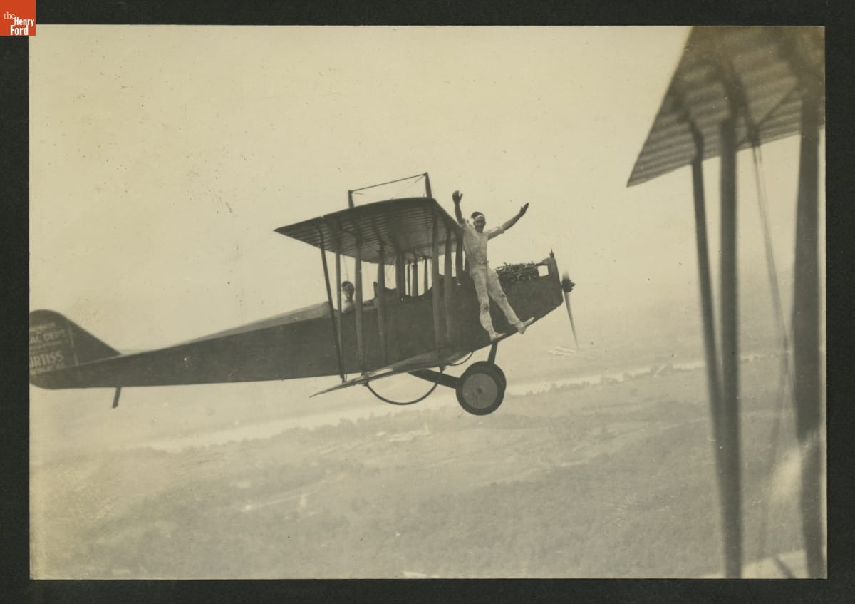 "Jersey" Ringel Performing a Stunt on an Airplane in Flight, circa 1921 Man with arms upraised standing outside airplane in front of wing in midair