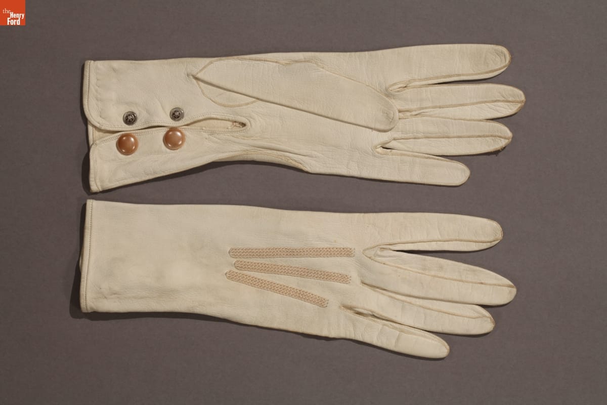 Pair of white gloves with elastic strips on top and buttons on underside