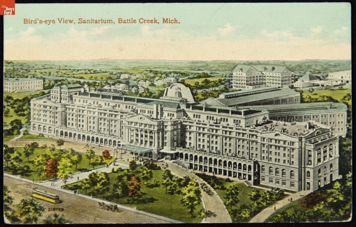 Color illustration of large white building complex surrounded by lawns, trees, and a few other buildings; contains text