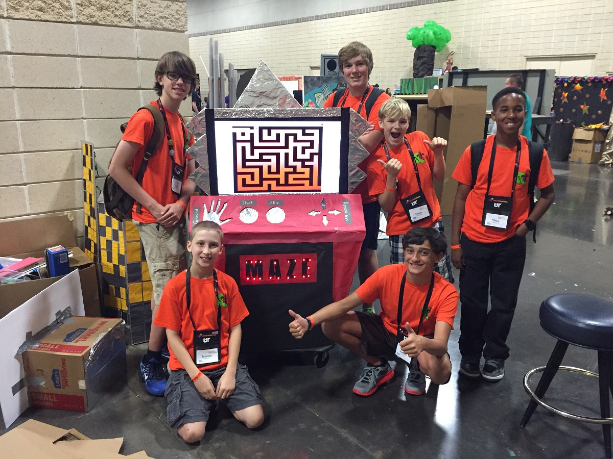 Spencer Kiper’s Destination Imagination team Group of children stand and kneel around an arcade game made out of cardboard