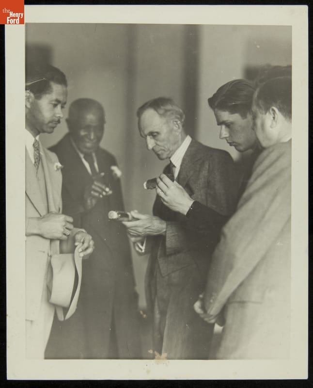 Five men in suits look at items some of them are holding in their hands
