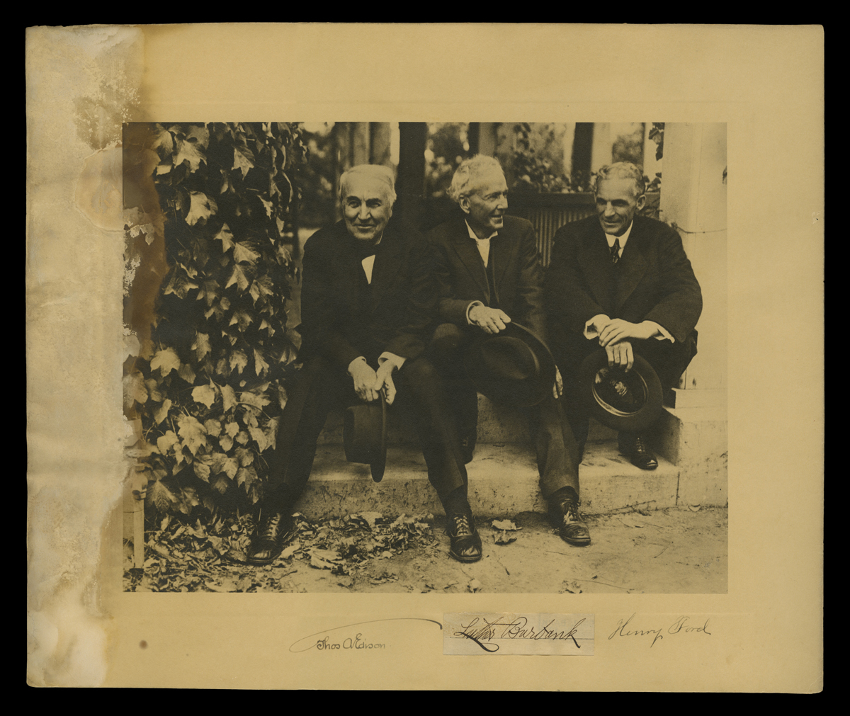 Three men in suits sit on steps next to an ivy-covered wall