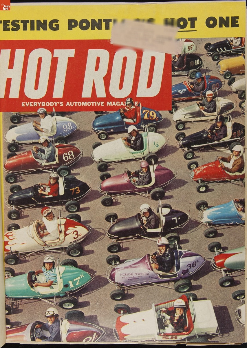 Magazine cover containing text and aerial photo of boys wearing helmets sitting in small open cockpit cars