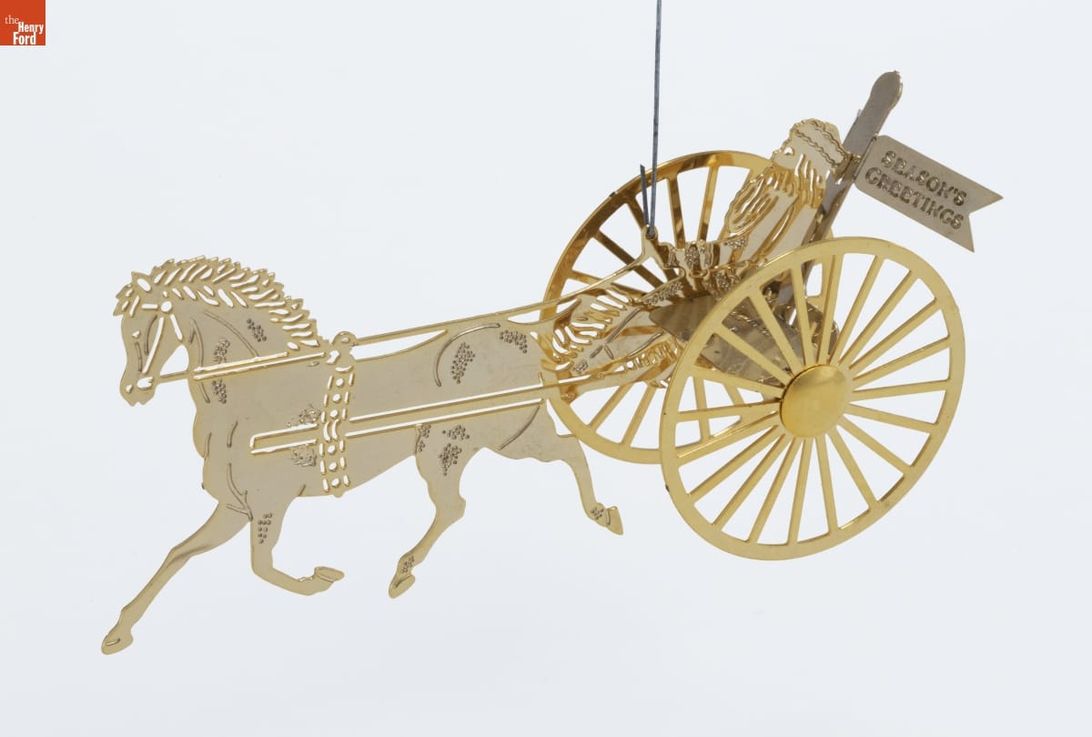 Gold and white metal ornament depicting Santa and a flag reading "Season's Greetings" in a wagon harnessed to a horse