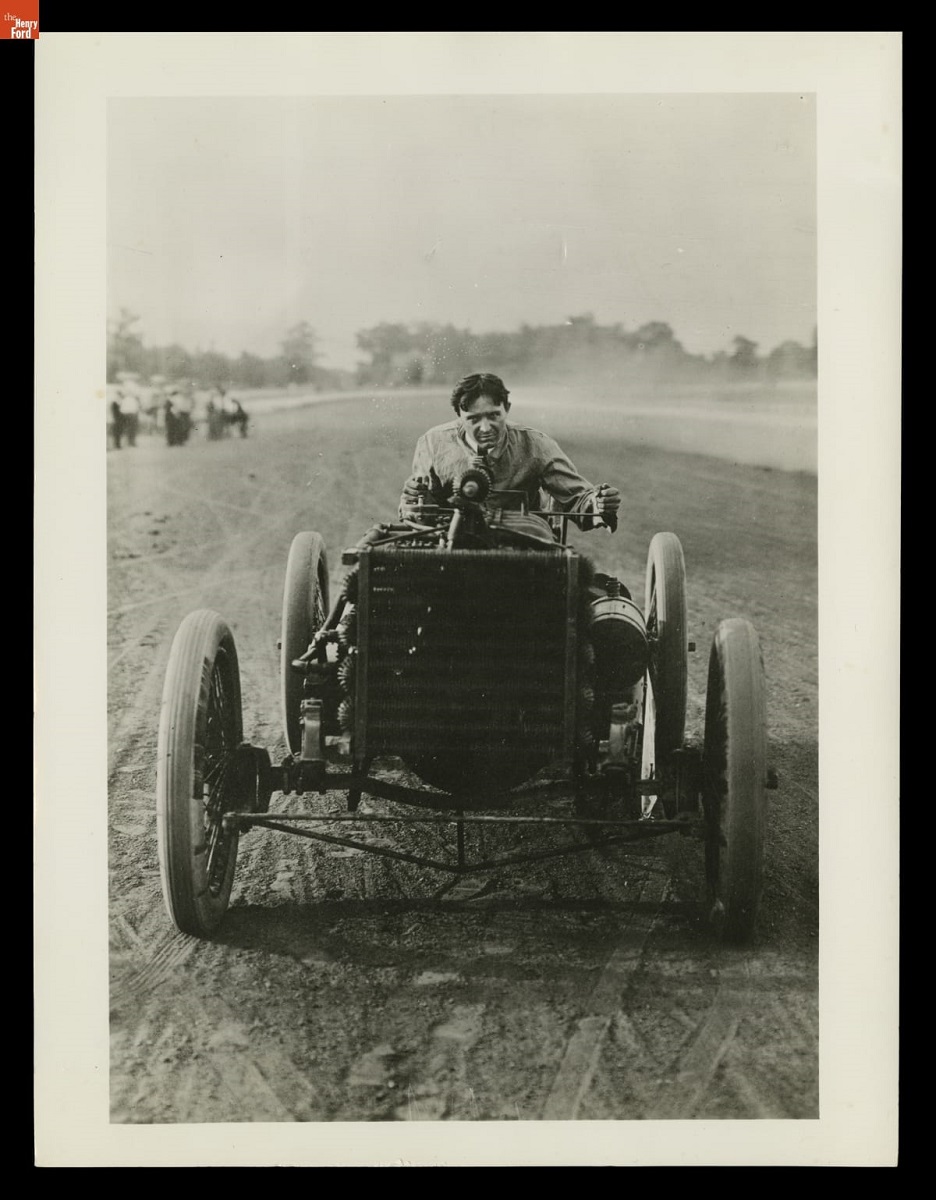 Barney Oldfield Driving the Ford "999" Race Car, circa 1903 Man crouches at wheel of an open early race car on a dirt track