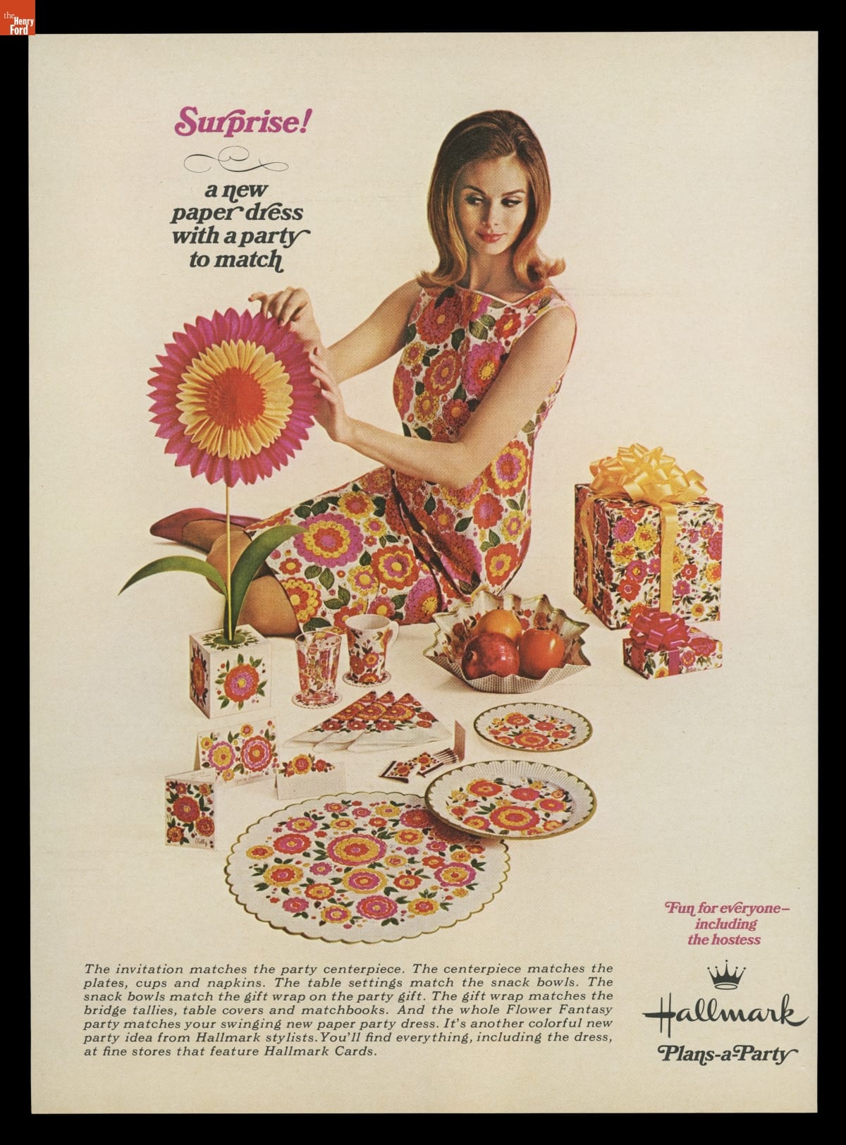 Seated woman wearing floral dress with matching floral tableware, decorative honeycomb paper flower and wrapped gift nearby