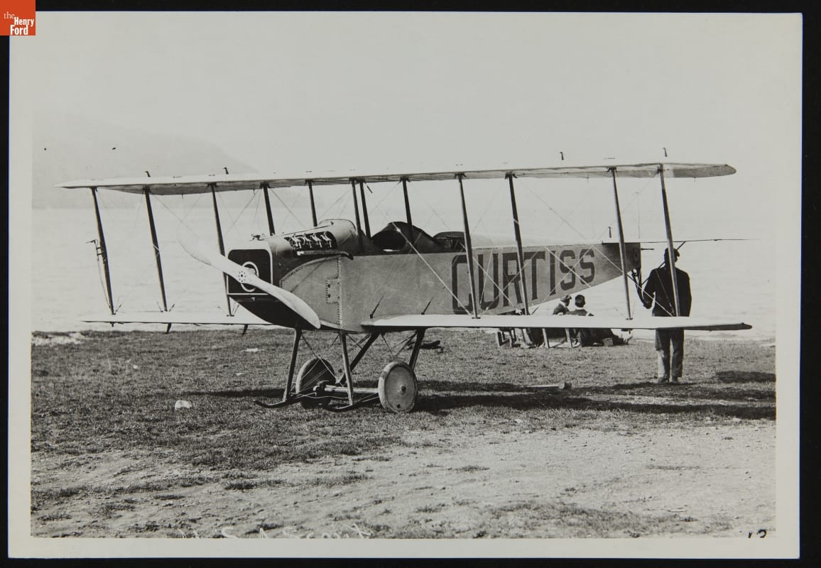Curtiss JN "Jenny" Airplane, circa 1915 Man standing at back of airplane with large text "CURTISS" painted on side