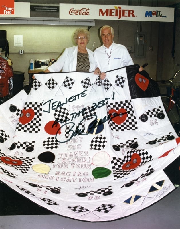 Jeanetta Holder Presents a Quilt to Roger Penske to Mark His 30 Years of Racing at the Indiapolis 500, 1999 Woman with blonde hair and glasses and man with white hair in a white dress shirt hold a quilt; text inscription and signature on photograph