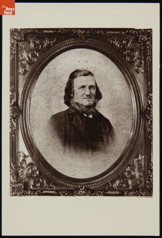 Portrait of man with shoulder-length hair and beard wearing suit, in ornate frame