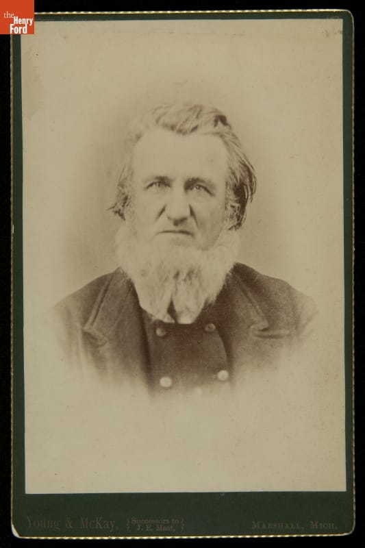 Man with hair brushed back and white beard, wearing jacket