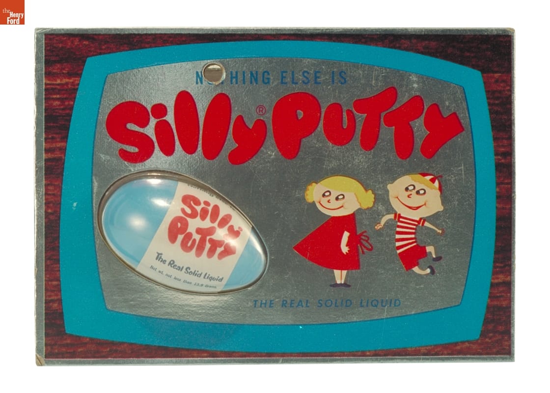 Silly Putty, circa 1962 Plastic blister pack containing blue plastic egg with red and white label "Silly Putty" against blue, silver, and woodgrain background with text