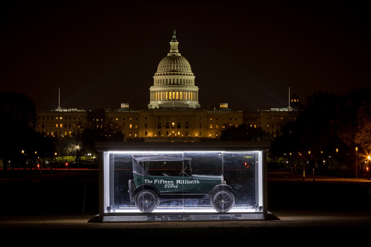 Green Model T car with writing on sides in a large glass case at night on a pathway with the U.S. Capitol lit up behind it
