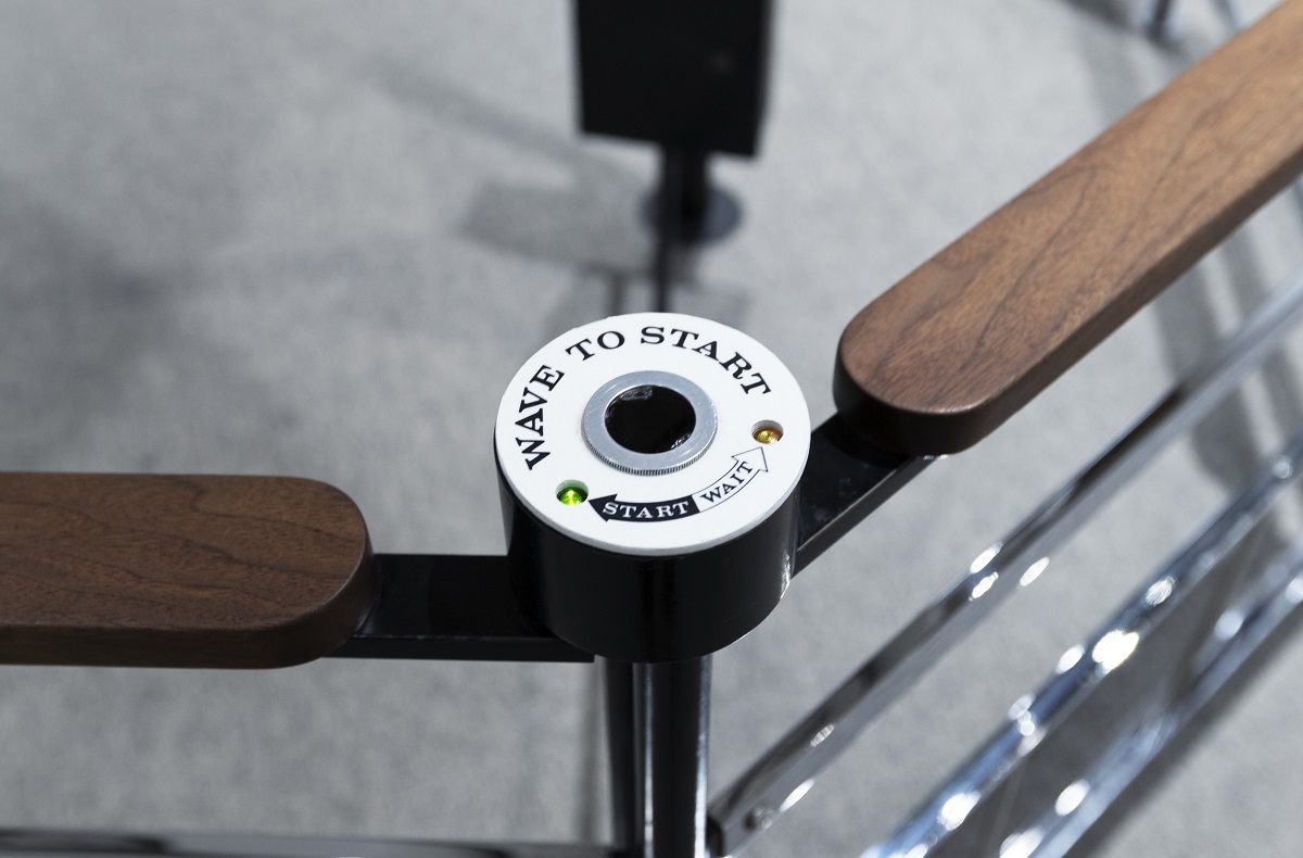 Metal and wood railing with a white sensor mounted on it, with text reading "WAVE TO START"