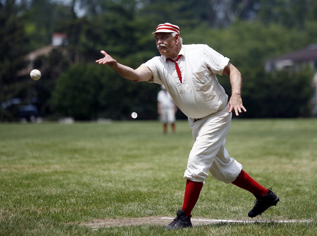 Historic Base Ball in Greenfield Village An historic base ball player in a white and red uniform throws a ball on a grassy field
