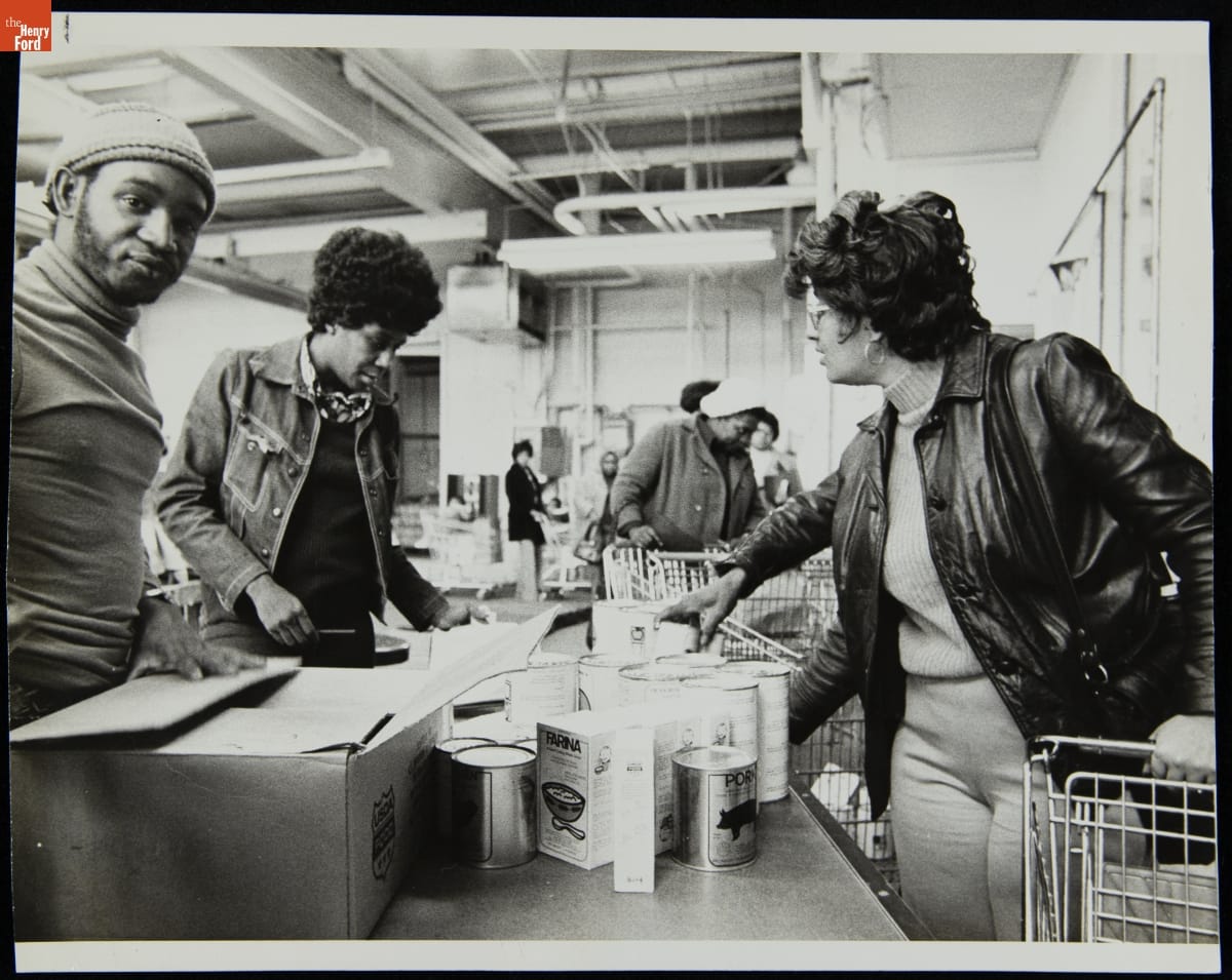 People of color stand by tables containing food in an industrial-looking space