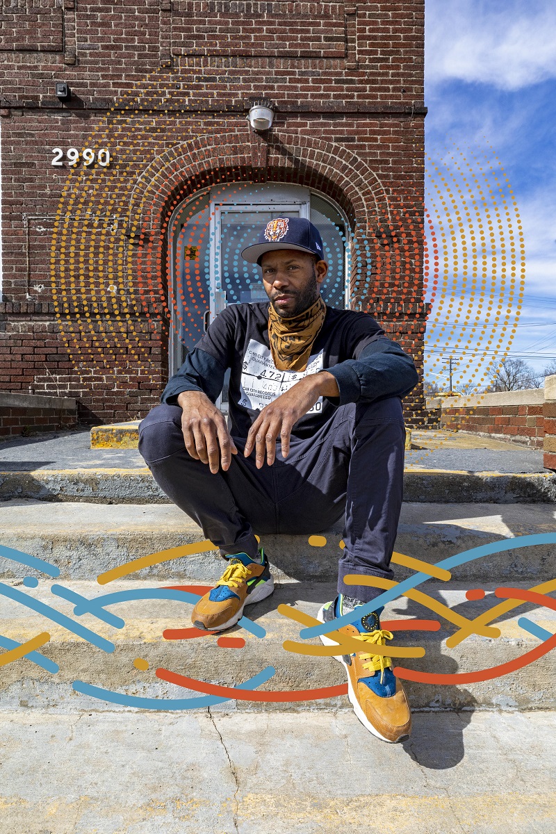 African American man sits on steps outside a red brick building; a colorful graphic of wavy lines has been added to the photo