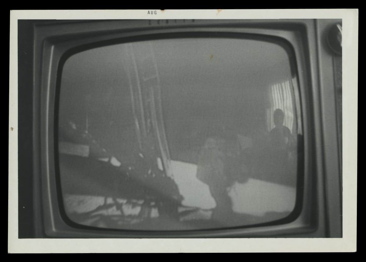 Black-and-white photograph of the moon landing on a TV set with watchers reflected in the glass