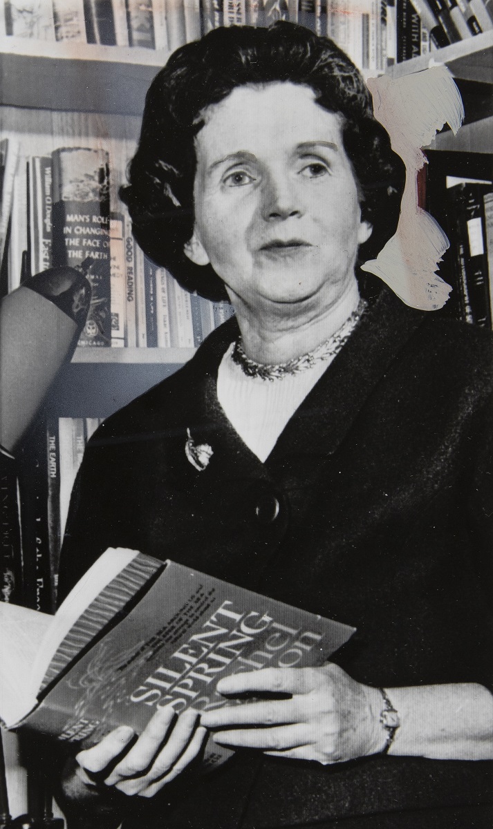 Black-and-white photo of woman holding book in front of bookshelves