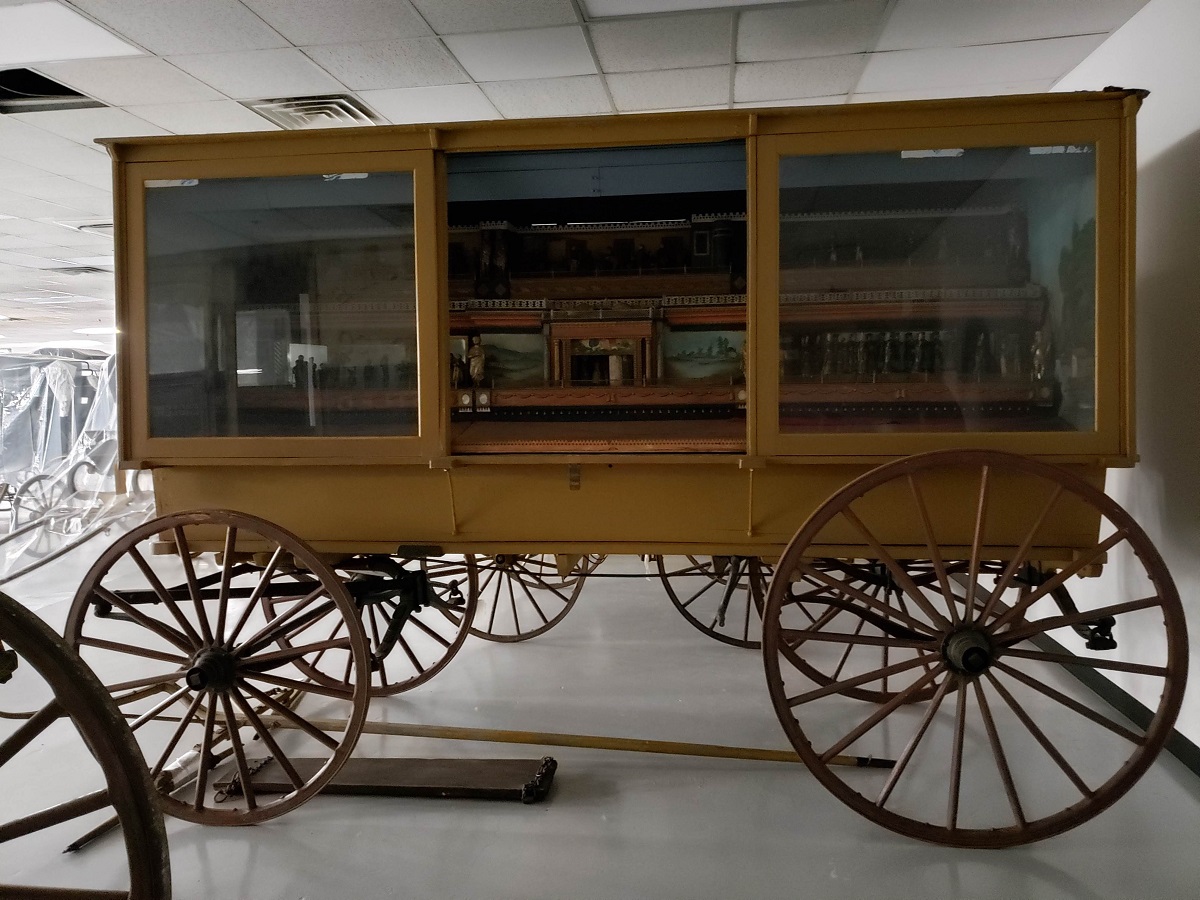 “The Busy World” automaton wagon in storage in MSB before photography Yellow wagon with glass windows revealing scenes on side