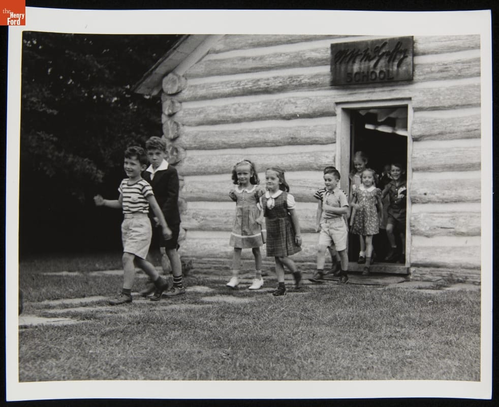 Group of children walk out of a log cabin door