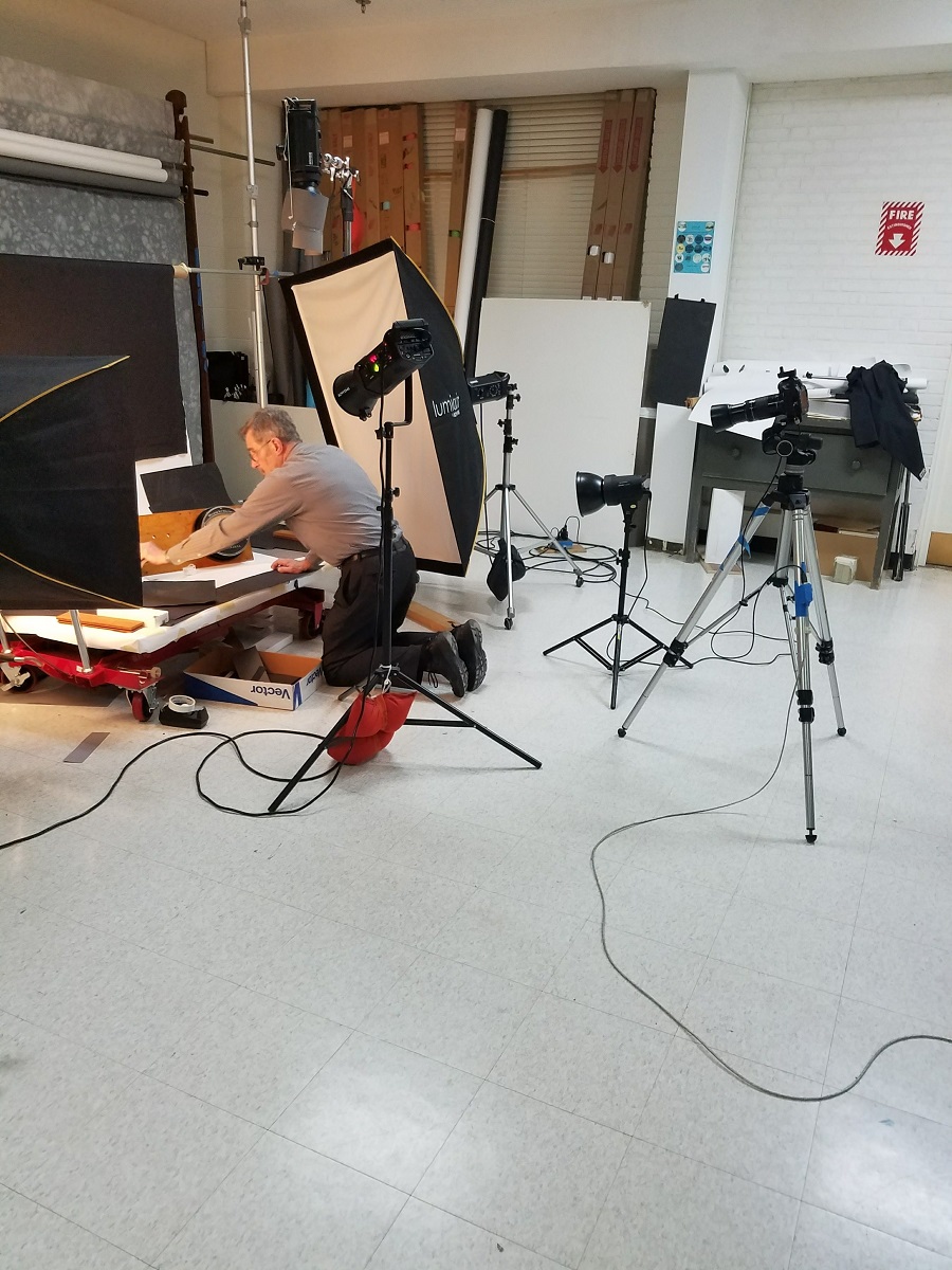 Photographer Rudy Ruzicska, photographing a meter in our former Photo Studio Man kneels and arranges a photo set with lights and camera pointing at it