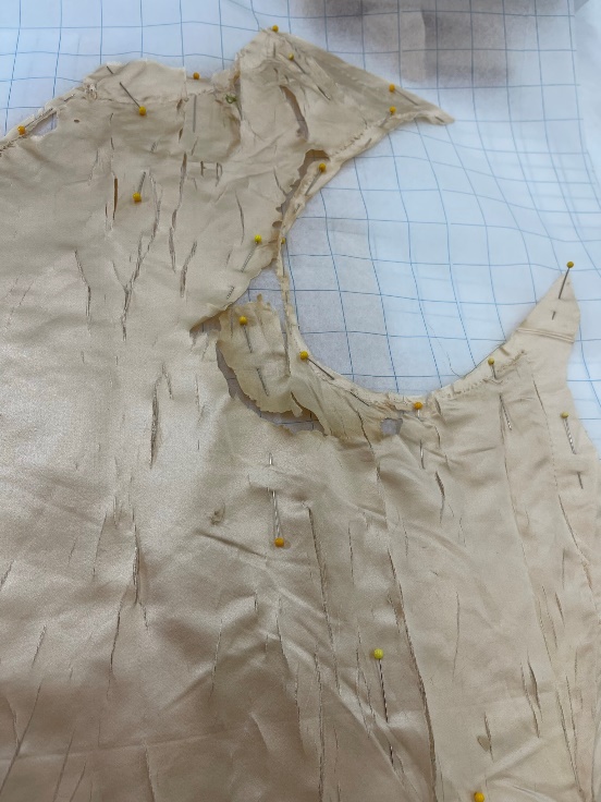 Cream silk fabric with many rips and gaps lays on top of gridded paper