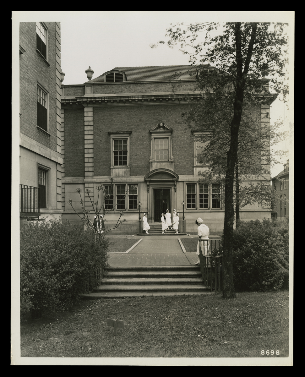 Entrance to brick building, with walkway and several people wearing nurses' uniforms outside