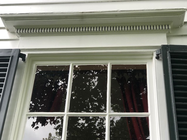 Decorative window lentil, ornamented with dentils, on the Noah Webster Home Top of a window, showing decorative trim above, and part of black shutters to either side; maroon curtains visible inside