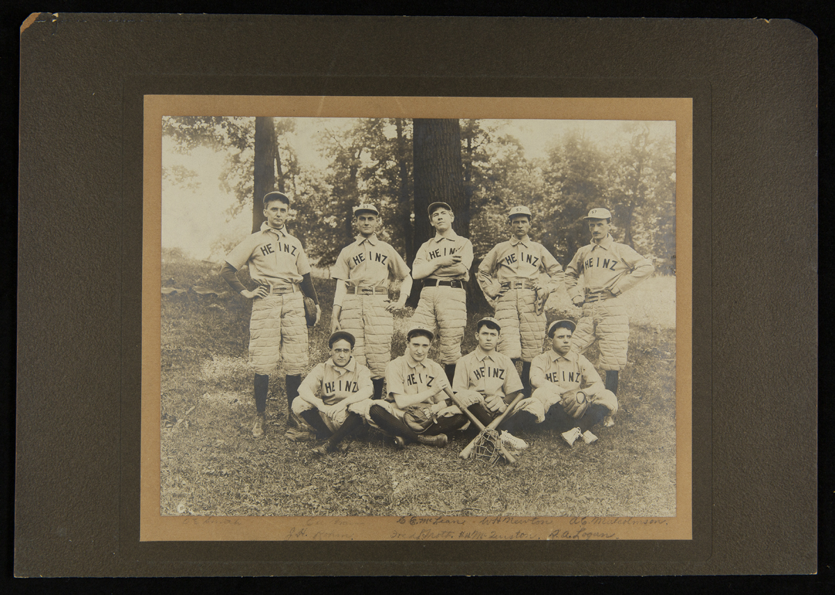 Group of nine men wearing baseball uniforms, some sitting and some standing, some with bats