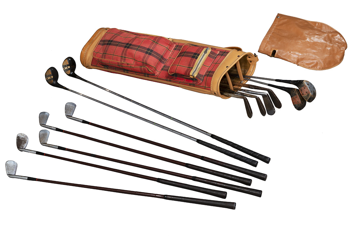 Golf clubs lying next to red plaid golf bag and brown leather bag cover
